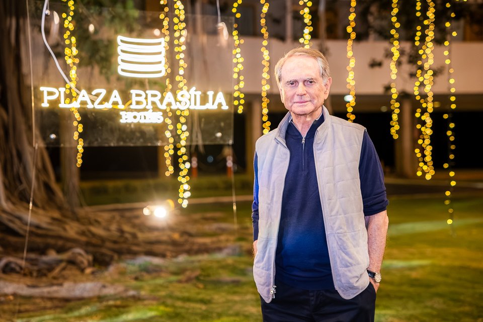 Paulo Octávio, de colete branco, sorri em frente ao letreiro iluminado do Plaza Brasília Hotéis durante o Arraiá do Brasília Palace.